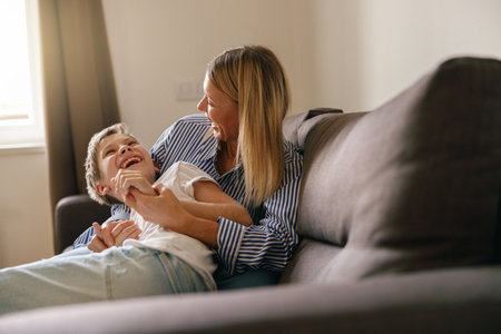Mother and son plays tickle at home on the sofa living room. Happy motherhood and childhoodの写真素材