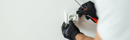 Close up of hands of male worker, professional electrician in protective gloves using screwdriver while installing new electrical socket outlet after renovation workの写真素材