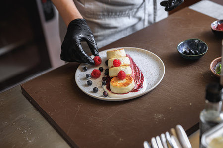 Kitchen worker decorated ready cheesecakes with berries for breakfast in restaurantの写真素材