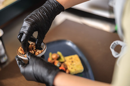 Kitchen workers hand is decorating the ready dish with nuts before servingの写真素材