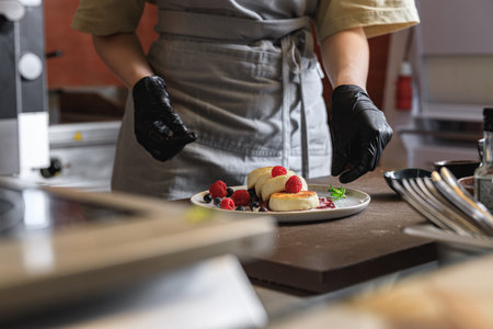 Kitchen worker decorated ready cheesecakes with berries for breakfast in restaurantの写真素材