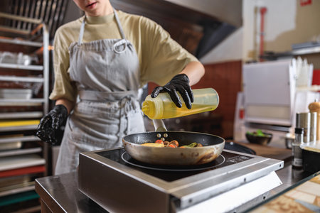 The professional chef in uniform adds oil into pan with dish in restaurant kitchenの写真素材