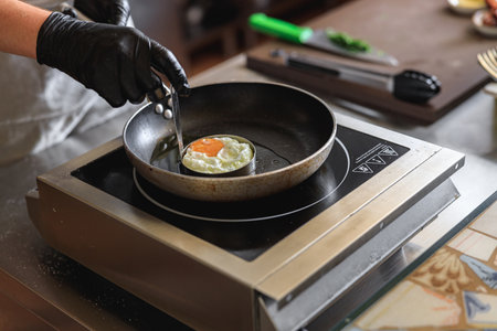 Professional kitchen worker cooking egg on a frying pan to make delicious breakfastの写真素材