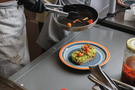 Chef hands cooking avocado toast with vegetables for breakfast menu in restaurant kitchenの写真素材