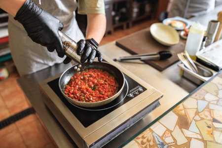 Close up of professional chef in uniform adds spices into pan with dish in restaurant kitchenの写真素材