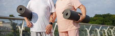 Mature couple in sportswear with mats ready for workout on footbridge at sunset closeupの写真素材