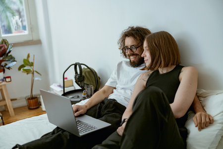 Young family watching TV series using laptop sitting on couch in cozy apartment. Couple in loveの写真素材