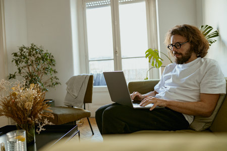 Young man freelancer sitting on sofa at home and working on laptop online. Remote work conceptの写真素材