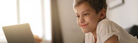 Young boy lies on the bed and looks into an open laptop. Home education conceptの写真素材