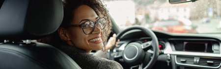 Woman driving car with one hand on steering wheel and another on gear lever and looking at cameraの写真素材