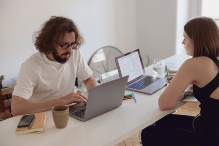 Married couple freelancers sit at table in living room with laptops and working from home office