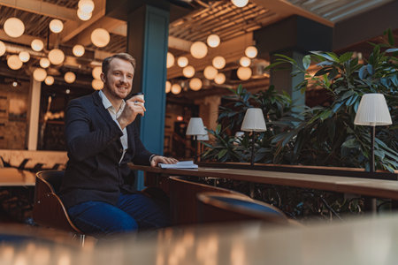 Smiling businessman holding a notepad and drinking coffee during working day in modern coworkingの写真素材