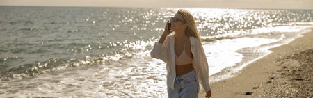 Pleased lady smiling while talking on the phone at sea coastの写真素材