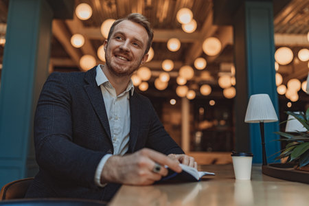 Smiling businessman holding a notepad and drinking coffee during working day in modern coworkingの写真素材