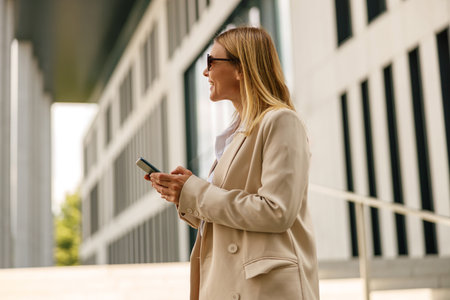Woman manager with phone standing on modern building background and looking at sideの写真素材