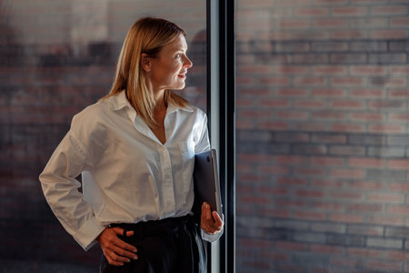 Smiling woman manager standing with laptop in coworking and looking at side. Distance work conceptの写真素材
