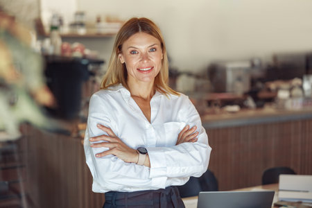 Stylish middle-aged businesswoman standing with crossed hands on coworking space backgroundの写真素材