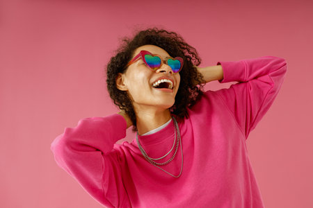 Smiling woman in sweater is touching hair and looking at side standing on pink studio background