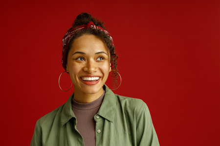 Portrait of charming woman looks away with smile standing on red studio background