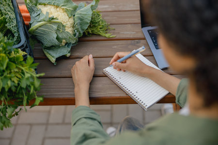 Close up of woman farm owner making notes in notepad with vegetables on backgroundの写真素材