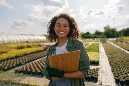 Positive woman farmer holding clipboard while standing on garden center backgroundの写真素材