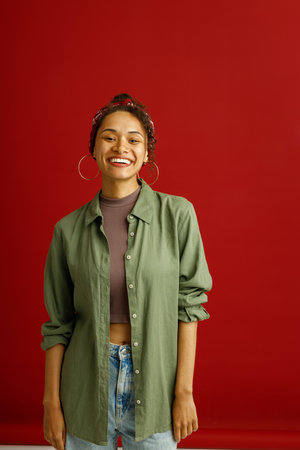 Pretty woman looks camera with smile while standing on red studio background
