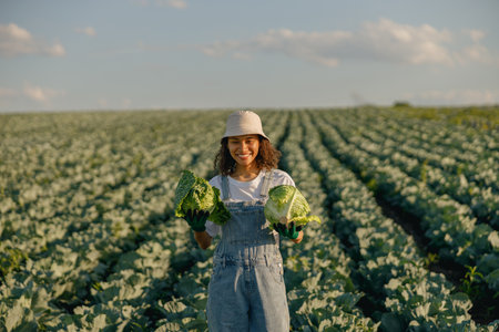 Smiling female farmer in uniform working in cabbage field during harvest. Agricultural activityの写真素材