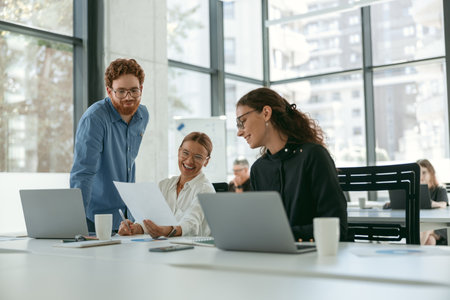 Group of young business people discussing something and smiling while sitting at the office tableの写真素材