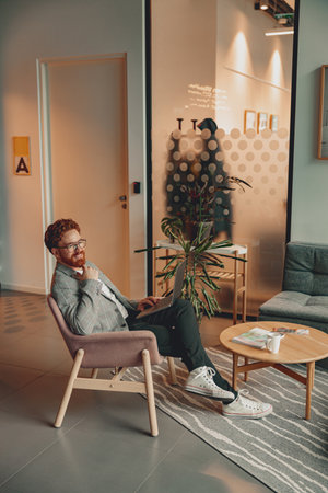 Smiling male sales manager in eyeglasses working on laptop sitting in office during working dayの写真素材