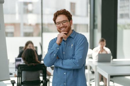 Handsome businessman in eyeglasses looking on camera with smile standing on office background