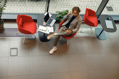 Top view of stylish male freelancer talking by mobile phone with client while sitting in coworkingの写真素材