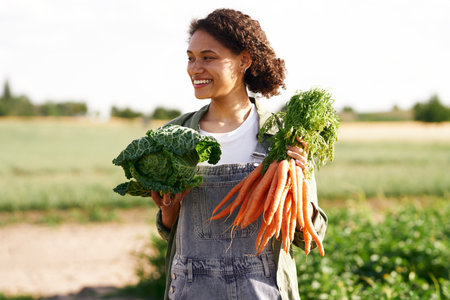 Cheerful female agronomist holding freshly picked carrots standing in field. High quality photoの写真素材