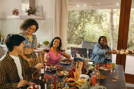 Group of smiling friends enjoying in conversation and drinking wine during Christmas party at homeの写真素材
