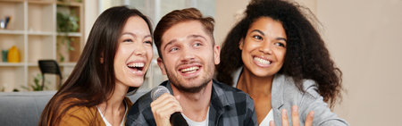 Karaoke singers. Three smiling friends looking happy while playing karaoke at home, singing with microphone, sitting on the couch in the modern apartmentの写真素材