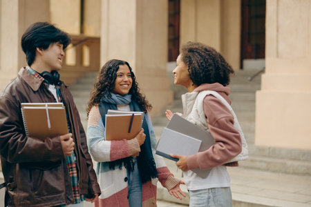 Young students talking and laughing together outdoor standing near campus and holding booksの写真素材