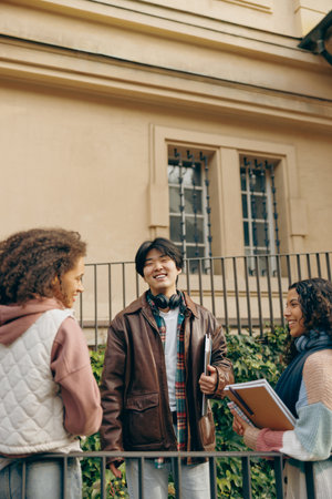 Happy students talking each other standing near university campus and holding books and laptopの写真素材