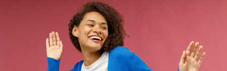 Happy woman in casual clothes dancing with raised hands while standing over red studio background