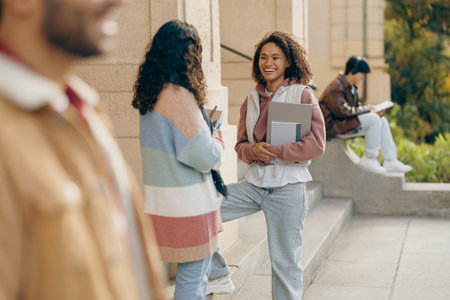 Happy students talking each other standing near university campus and holding books and laptopの写真素材
