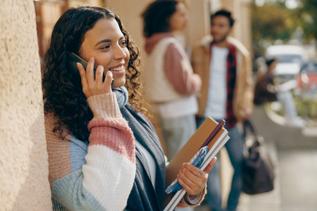 Smiling female student talking on phone standing near university on friends background