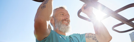 Strong and healthy people. Happy bearded senior man pulling up on horizontal bar and smiling while training outdoors. He is working out at the stadium. Morning exercisesの写真素材