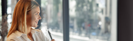 Smiling mature business woman standing with crossed hands in modern coworking and looking at sideの写真素材