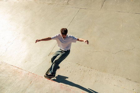 Full body of young male skater in casual outfit doing trick on skateboard riding in skate parkの写真素材