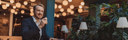 Smiling businessman holding a notepad and drinking coffee during working day in modern coworkingの写真素材