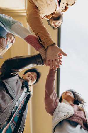 Bottom view of friendly young students putting their hands together standing near campus buildingの写真素材
