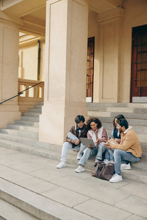 Happy students sitting on stairs, looking at laptop and discussing their project together