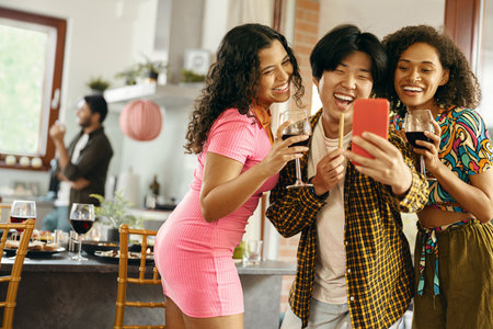 Smiling young friends taking selfie photo holding wine glasses on holiday dinner party at homeの写真素材