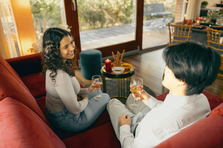 Two smiing diverse friends talking and drink wine during holiday party at homeの写真素材