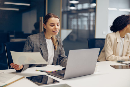 Stylish female freelancer working with documents and use laptop while sitting in modern coworkingの写真素材