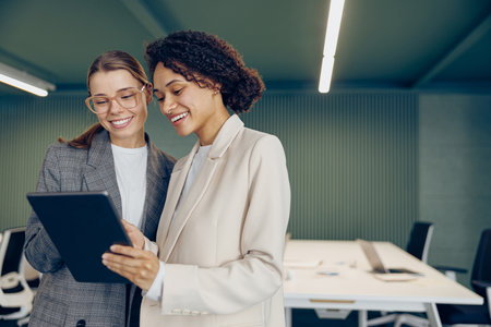 Two busy female coworkers discussing project standing in modern office and use digital tabletの写真素材