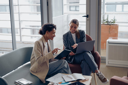 Two young female coworkers talking during business meeting in cozy office. Teamwork conceptの写真素材